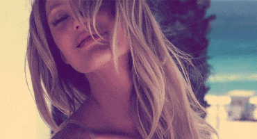 Celebrity gif. Candice Swanepool laughs while posing for a Victoria's Secret photoshoot.