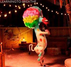 Movie gif. Dressed as a clown with a large rainbow afro, and colorful dots on his body, Marty the Zebra from Madagascar dances, hopping on his hind legs and turning, waving his arms.
