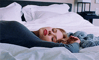 Movie gif. Scarlett Johansson as Charlotte in Lost in Translation. She's laying on a bed with her arms above her head and looks bored before turning her head away.