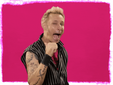 Celebrity gif. Mike Dirnt from Green Day stares at us with a turtle-like smile, covering his teeth with his lips. He raises up a big thumbs up. 