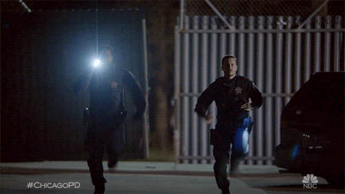 TV gif. Two officers from Chicago PD are running in the dark with their flashlights brandished.