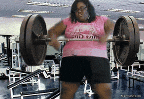 Video gif. Large woman wearing a pink shirt the reads "Diva girl," in a gym, lifting a large barbell, slamming it up and down with ease, as if dancing.