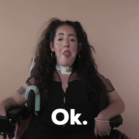 Reaction gif. A Disabled white woman with muscular dystrophy with wavy brown half up half down with two pigtails on top, seated in her motorized wheelchair, says dispassionately, "Ok."