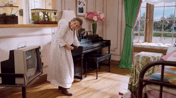 TV gif. Amy Sedaris dressed as an old woman on At Home With Amy Sedaris dances joyfully in a bedroom, holding her skirt up so she can tap dance as she laughs and smiles. 