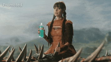 Sponsored gif. Aubrey Plaza has her hair in two long braids and wears a brown leather armored dress. She rides on a flying dragon holding onto one of its horns with her left hand. She turns to us slowly with a deadpan gaze while holding a Mountain Dew Baja Blast in her right hand.