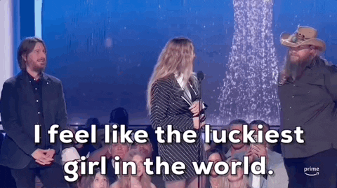 ACM Awards gif. Woman accepting award turns head around to speak into the microphone and says "I feel like the luckiest girl in the world" with a smile on her face while holding a trophy two male presenters stand behind her listening tentatively. 