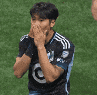 Sports gif. Jeong Sang-bin of Minnesota United gasps in shock as he covers his mouth with both hands while standing on a soccer field.