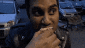 Celebrity gif. Aziz Ansari takes a bite of a pastry and scrunches his eyes in pleasure. We can nearly hear his moan as he chews and swallows, and it looks like the most delicious thing ever.