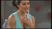 Video gif. Elissa Slater from Big Brother takes a sip of water from a white coffee mug and something in front of her makes her laugh. She sprays water out of her mouth as she doubles over laughing.