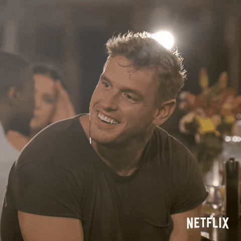 Reality TV gif. Shayne Jansen on Love is Blind sits hunched over, looking over his shoulder and smiling for a moment before his jaw drops in shock. 