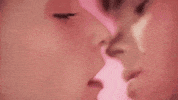 Video gif. Teenage boy and girl lean in for an intimate kiss; the girl reaches out for the boy’s neck as the boy runs his fingers behind her ear.