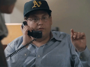 Movie gif. Jonah Hill as Peter Brand in Moneyball sits with anticipation on the phone, then clenches his fist with a look of satisfied victory.