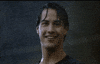 Movie gif. Keanu Reeves as Johnny Utah in Point Break smiles and gives a cool thumbs-up while standing soaking wet from the pouring rain around him.