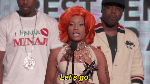 Celebrity gif. Nicki Minaj holds an award, standing behind a mic at a BET awards show, saying "let's go" and then beginning to walk off.