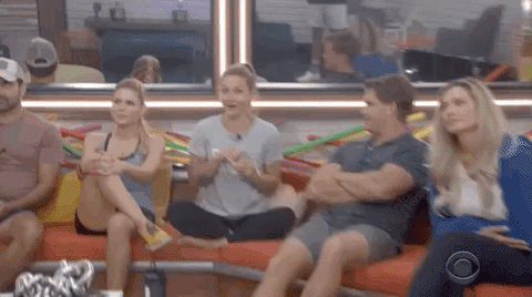Reality TV gif. A contestant on Big Brother is sitting cross legged on the sofa and the camera pans on her and zooms in while she chuckles heartedly, having heard some good tea.