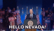 Political gif. Joe Biden stands at a podium in front of American flags and a crowd of supporters holding signs that read, "Biden Harris" and "Vote!" He says, “Hello Nevada!”