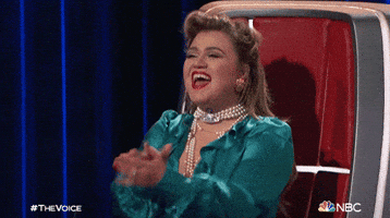 TV gif. On an episode of "The Voice," judge Kelly Clarkson claps and cheers joyfully from her judge's chair.