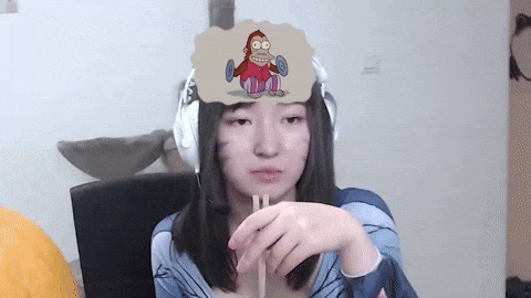 Video gif. A woman with cat whiskers painted on her cheeks wears headphones and stares off into space while holding a pair of chopsticks. A thought bubble contains a monkey clapping some cymbals together and doing backflips. 