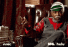 SNL gif. Jay Pharoah wears a tracksuit and a gray mustache as he sits in a tufted leather armchair and gestures to a pile of money on a table beside him.