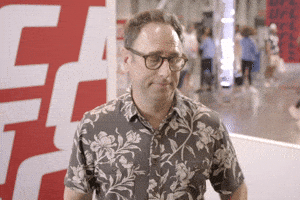 Celebrity gif. Jason Sklar looks at his watch and points at it, then points at us.