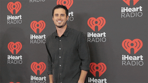 Celebrity gif. Ben Higgins is on the red carpet at the iHeartRadio Festival and he waves at us and smiles charmingly.