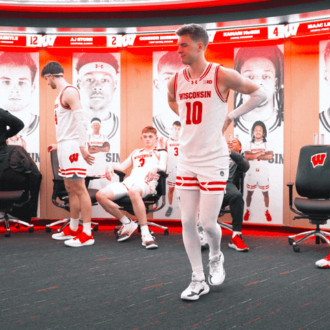 Sports gif. Wisconsin Badgers basketball player Isaac Lindsey dances like a chicken while hanging out with team mates who are watching in the background. He has a smile on his face and is wearing his #10 uniform. 