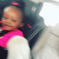 Video gif. Baby buckled into a car seat smirking and dancing to a beat until she suddenly stops and her eyes get wide.
