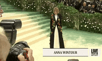 Met Gala 2024 gif. Long zoom in on Anna Wintour posing for the cameras wearing a custom Loewe jacket adorned with colorful oversized flowers and her signature knowing smirk.