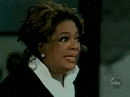 TV gif. Oprah Winfrey stares straight ahead with wide eyes and a forced smile through gritted teeth. Her eyes quickly flash to one side before looking back like she's extremely uncomfortable with what's happening. 