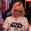 Celebrity gif. Emma Fyffe, wearing a Star Wars shirt, recoils in retrained dubiety, with a laugh of incredulity.