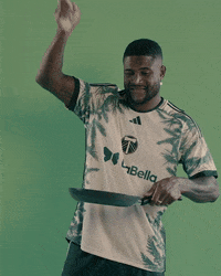 Sports gif. Dairon Asprilla of the Portland Timbers wears his jersey as he smiles and holds a frying pan, pretending to cook in the pan.