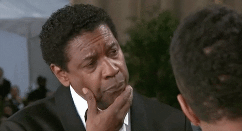 Celebrity gif. Denzel Washington is being interviewed on a Red Carpet event. He looks away with tight lips and rubs his chin as he ponders the question he’s been asked.