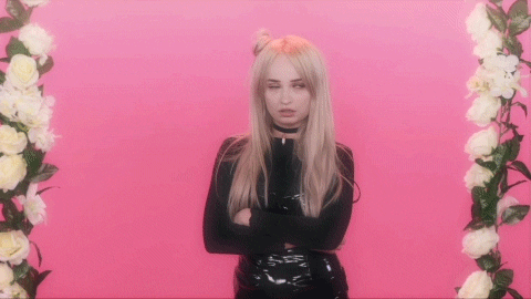 Celebrity gif. Kim Petras stands with her arms crossed in front of a vibrant pink backdrop with white floral decorations on each side. She is completely over it, rolling her eyes dramatically and looking off to the side.