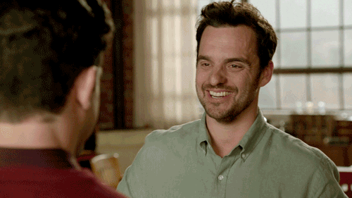 TV gif. Jake Johnson as Nick in New Girl, smiles as he walks towards us and high fives Max Greenfield as Schmidt who is mostly off screen. 
