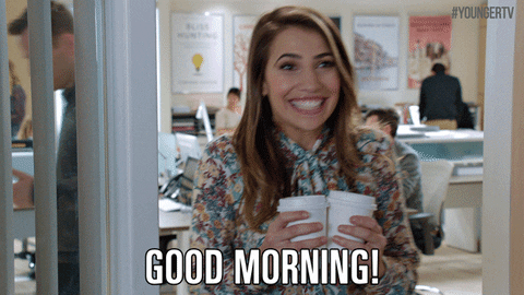 TV gif. Sutton Foster as Liza on Younger, in an office doorway, holds two takeout coffee cups with both hands and grins enthusiastically as she says "Good morning!" which appears as text.