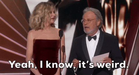 Nodding his head and spreading his hands, Billy Crystal says “Yeah, I know, it’s weird.” Meg Ryan stands next to him, first watching him and then smiling.