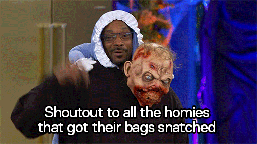 Celebrity gif. Wearing a Halloween costume that makes him look like a baby riding on a zombie’s back, Snoop Dogg holds up his hand and says with a smile, “Shoutout to all the homies that got their bags snatched.”