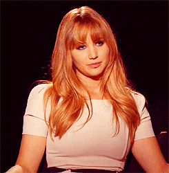 Celebrity gif. Actress Jennifer Lawrence wryly smiles during an interview with an annoyed expression on her face.