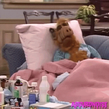 TV gif. Alf laying up on a couch, surrounded by pillows and blankets and many different bottles of cold medicine, sneezing into a tissue.