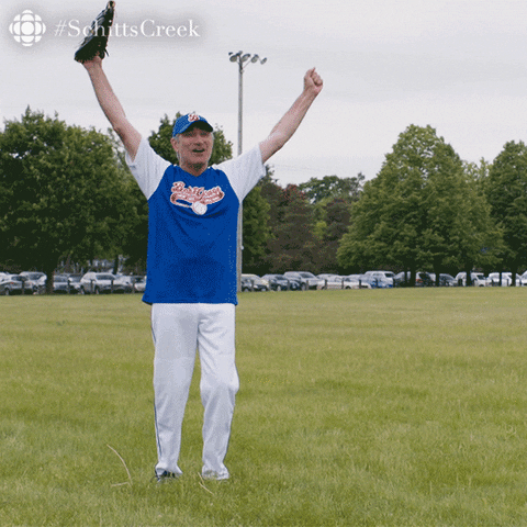Schitt's Creek gif. Eugene Levy as Johnny. He's wearing a baseball jersey and throws his arms in the air as he celebrates and points, saying, "That's my boy!"