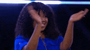 Reality TV gif. Niecy Nash on "Don't Forget the Lyrics" stands and claps, smiling proudly as lights on set flash behind her.