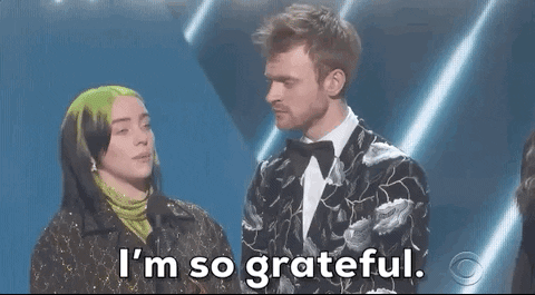 Celebrity gif. Billie Eilish and Finneas O’Connell stand on stage at the Grammys with an award in Billie’s hands. Finneas looks at Billie as she says, “I’m so grateful.”
