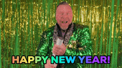 Video gif. Man wearing a sparkly green suit in front of a golden and green shiny background. He smiles at us and holds a confetti in his arms, letting it pop. Confetti falls in front of him. Text, “Happy New Year!”