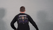 Video gif. Man jumps and turns towards us, landing with two thumbs up and a sarcastic expression on his face.