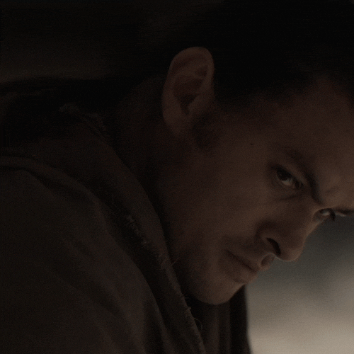 Movie gif. Jason Momoa as Duncan in Dune is close up in a dark room as he turns and looks off with an extremely serious gaze.