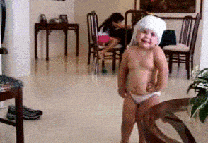 Video gif. A toddler in a diaper with a towel on their head dances as they clap and shake their hips.