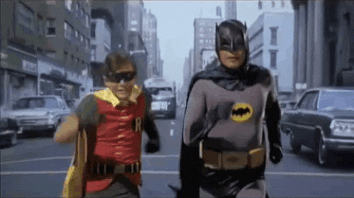 TV gif. With determination, fully costumed and masked Batman and Robin run toward us.