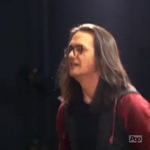 Reality TV gif. A man on Sing It On jumps up and down. His long hair bounces up and down with him. He excitedly says, “Yes, that’s awesome!”