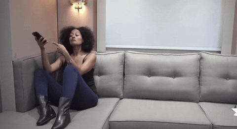 Celebrity gif. Tracee Ellis Ross sits on a couch while looking at her phone. She points her phone and then looks at us with wide eyes.