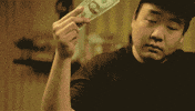 Video gif. David Cho, a Youtuber, is doing a shoulder dance and looks swaggy. He holds a one dollar bill in one hand and makes it rain, with one single dollar bill.